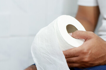 Man suffers from diarrhea hand hold tissue paper roll in front of toilet bowl. constipation in bathroom. Treatment stomach pain and Hygiene, health care