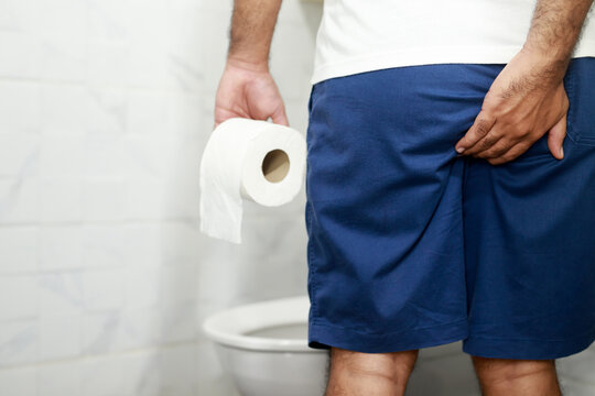 Man suffers from diarrhea hand hold tissue paper roll in front of toilet bowl. constipation in bathroom. Treatment stomach pain and Hygiene, health care