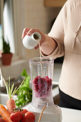 Plus-size woman pouring non-dairy mink in blender with cut red dragon fruit