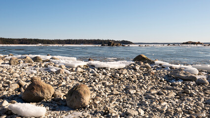 Snow and ice covered granite stones in front of an ice covered sea in winter under a blue sky
