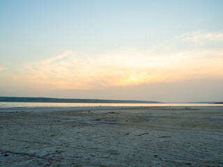 Dried up sandy estuary under the boundless sky. Twilight on the salt lake beach.