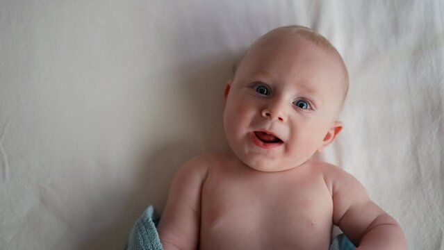 Little cute causian baby boy with blue eyes smiling and lying on bed at bedroom. With copy space . Looking at camera.
