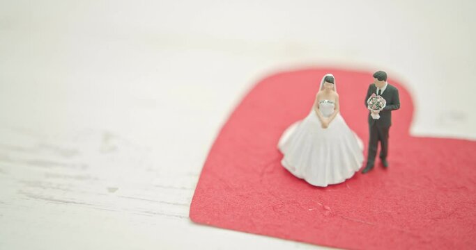Wedding and eternal love concept : Miniature figurine couple wedding doll, bride and bridegroom with a bouquet stand on a red mulburry paper heart.