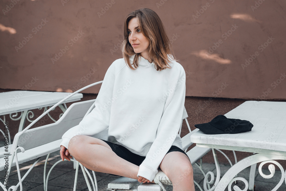 Wall mural Woman in white hoodie is sitting outdoors, mockup.