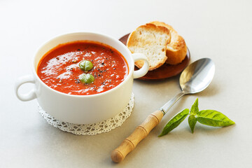 Italian tomato soup with croutons and basil on the table with a spoon.