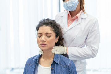Fototapeta premium Endocrinologist examining throat of young woman in clinic. Women with thyroid gland test . Endocrinology, hormones and treatment. Inflammation of the sore throat