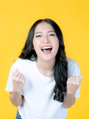 Portrait of excited beautiful happy Asian woman with happiness celebrating success isolated on yellow background