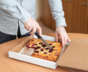 a man is cutting a pie with berries in the office, The pie is in a cardboard box for delivery.