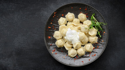 Ukrainian dumplings with sour cream and microgreen, on a black glossy plate, on a dark background