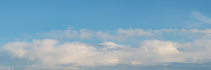 Panoramic view over soft blue sky with illuminated by sun rainy clouds as a background banner.