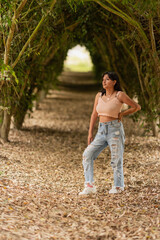 Naklejka premium Woman standing in a tunnel of trees with fallen leaves on the ground