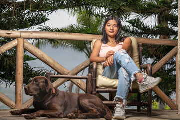 Latina woman sitting on a chair next to a dog on a terrace outdoors