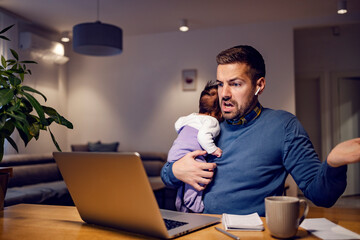 A confused busy father carry his baby girl and having video call with colleagues at home.