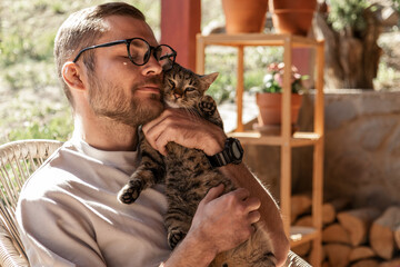 Happy handsome young adult man in glasses cuddles his cute cat. 