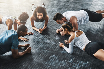 Planking - so simple, so effective. Shot of a group of young people doing planks together during their workout in a gym.