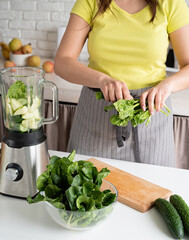 Young woman making green spinach smoothie at home kitchen