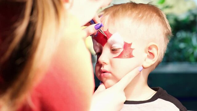 A little boy is put face painting on his face, his face is painted with paint. The concept of children's holiday, childhood, entertainment event, Halloween