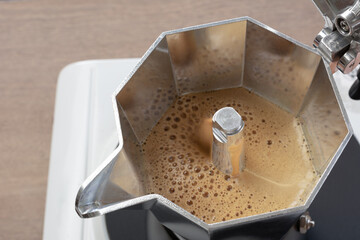 close up view of brewing espresso coffee with moka pot maker boiling on electric hot plate stove.