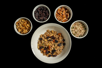 bowl of dry bran flakes with seeds nuts and rasins isolated on black