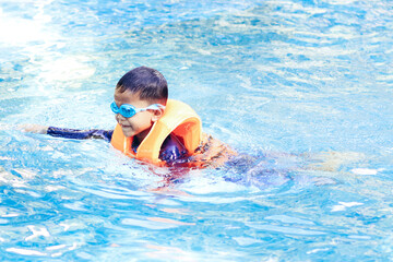 Fototapeta na wymiar Cute boy wearing safety inflatable armbands swimming in swimming pool