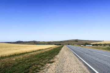 Fototapeta na wymiar Empty asphalt road between steppes on a background of blue sky in the village of Savvushki, Gorny Altai, Siberia, Russia. Summer time