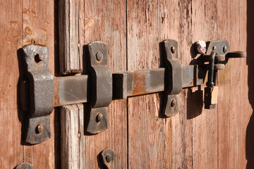 An old steel black and rusty latch lock on the wooden door. On the end is a padlock. Close-up shot