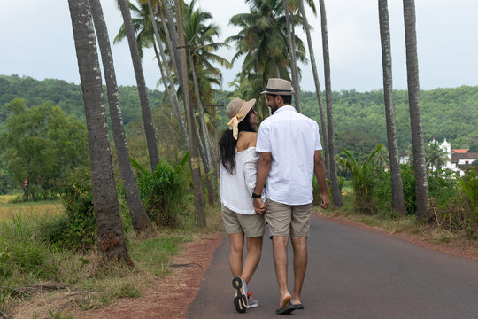 A beautiful young lovely attractive couple looking at each other, embracing, making love, smiling, cuddling walking on a famous Parra Coconut road in Goa surrounded by or lined with palm trees fields.