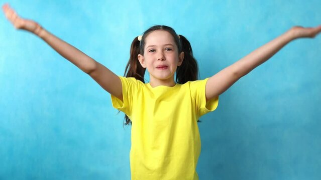 Beautiful little girl sends an air kiss and makes her hands a heart on a blue background