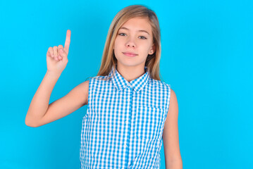 little kid girl with glasses wearing plaid shirt over blue background  showing and pointing up with fingers number one while smiling confident and happy.