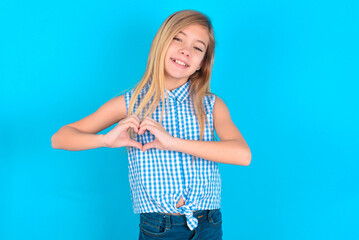 little kid girl with glasses wearing plaid shirt over blue background  smiling in love showing heart symbol and shape with hands. Romantic concept.