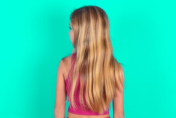 The back view of blonde little kid girl wearing pink sport clothes over green background Studio Shoot.