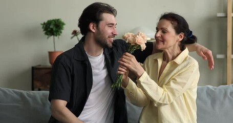 Caring grownup son congratulate surprised excited mature mom with Mothers Day give bunch of tender flowers with best wishes. Grateful touched old age mum receive bouquet from beloved child on March 8