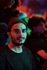 Portrait of content young Arabian gamer in eyeglasses participating in esports league, neon light