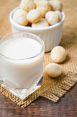 Macadamia milk in a glass and a bowl of macadamia nuts on a wooden background.
