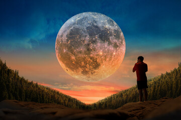 Young man is watching the full moon on a beautiful sunset. - obrazy, fototapety, plakaty