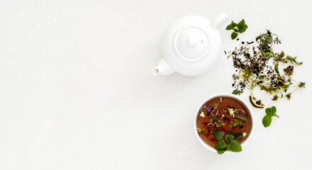 two white cups of tea with mint, dried medicinal herbs, next to a white teapot for brewing a drink,...