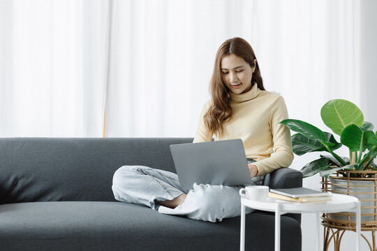 Woman plays on laptop on the sofa in her living room at home, she is resting on weekends after a hard day's work, she relaxes by watching movies and listening to music on her tablet. Holiday concept.