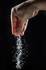 Fototapeta na wymiar Male hand sprinkling edible salt at black background.