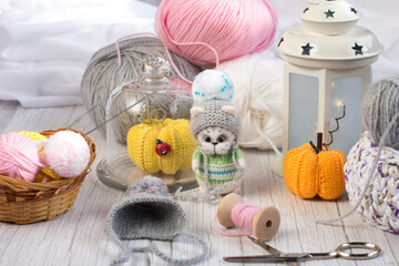 Fototapeta na wymiar a knitted kitten with knitting needles and orange pumpkins, colored balls of thread in a basket. Creative workshop on handmade needlework