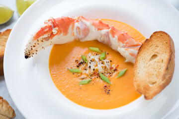 White plate of bisque served with a boiled crab claw, selective focus, close-up, horizontal shot