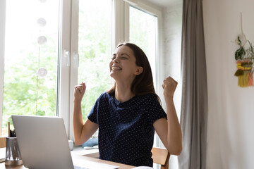 Cute woman celebrate great news read on laptop sit at desk with fists clenches looks excited feel...