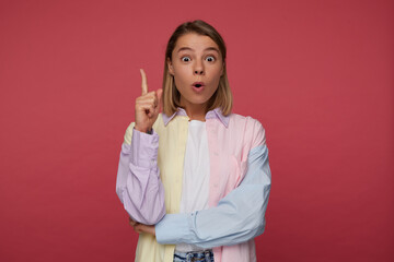 studio portrait of young female posing over red background, wears bright shirt point upwards with a...