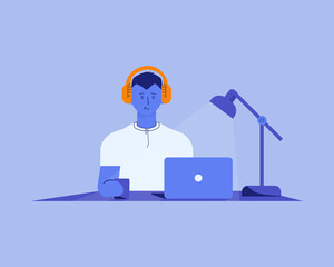 a man in headphones at his desk works in a laptop, drinks coffee or tea under a table lamp