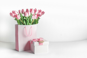 Present setting with pink tulips in shopping bag and gift box at white background. Celebrating in...