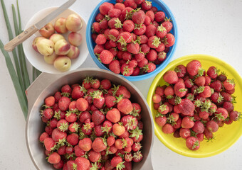 top view of fresh strawberries in bowls next to a bowl of peaches and green onions.