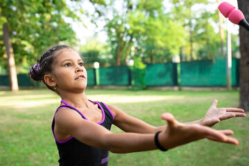 Girl doing exercise with clubs on rhythmic gymnastics training outdoors in summer in sports camp