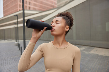 Active sporty brunette woman feels thirsty after workout drinks fresh water from bottle tired after...
