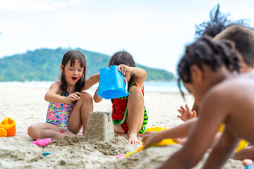 Group of Diversity little child boy and girl friends sitting on the beach playing sand with beach toy together on summer vacation. Happy children kid enjoy and fun outdoor lifestyle on beach holiday