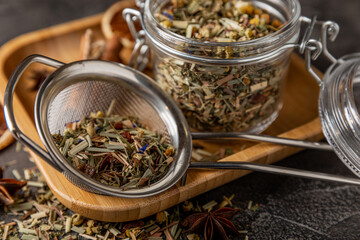 Herbal tea in a brewing strainer on a black textured background. Detox and tea for immunity. Herbal collection of chamomile, mint, lemon balm. pieces of wild rose and dried fruits.
