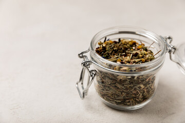 Green fragrant tea leaves in a glass jar on a gray textural background. Side view. Place for text